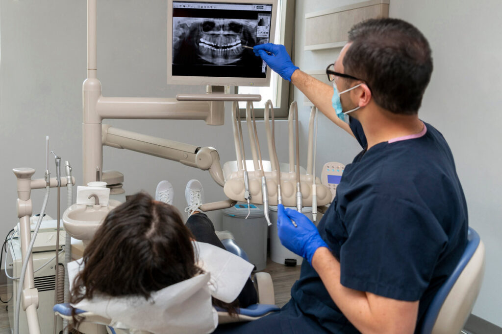 dentist gives information to her patient by showing dental x-ray showing. Medical teeth care taker pointing at patient radiography on screen. Tooth removal concept. Dental implants concept.