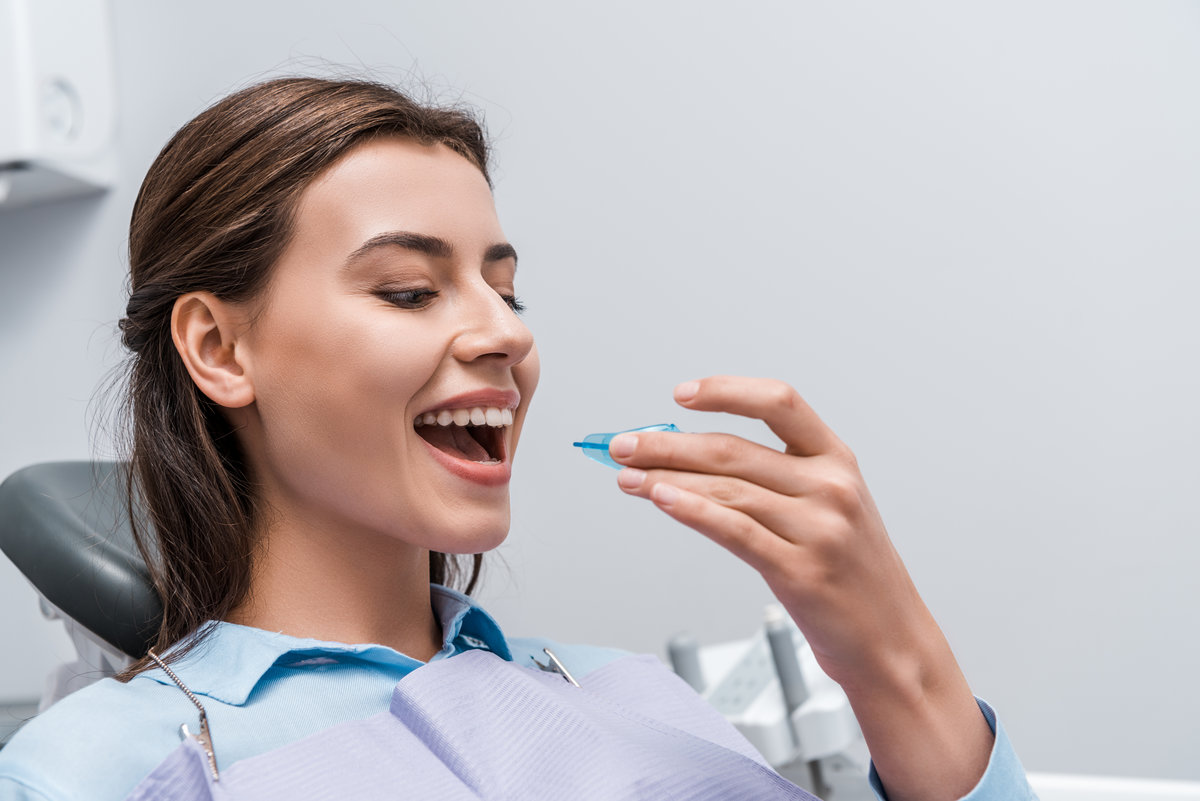 cheerful woman with opened mouth holding retainer in dental clinic