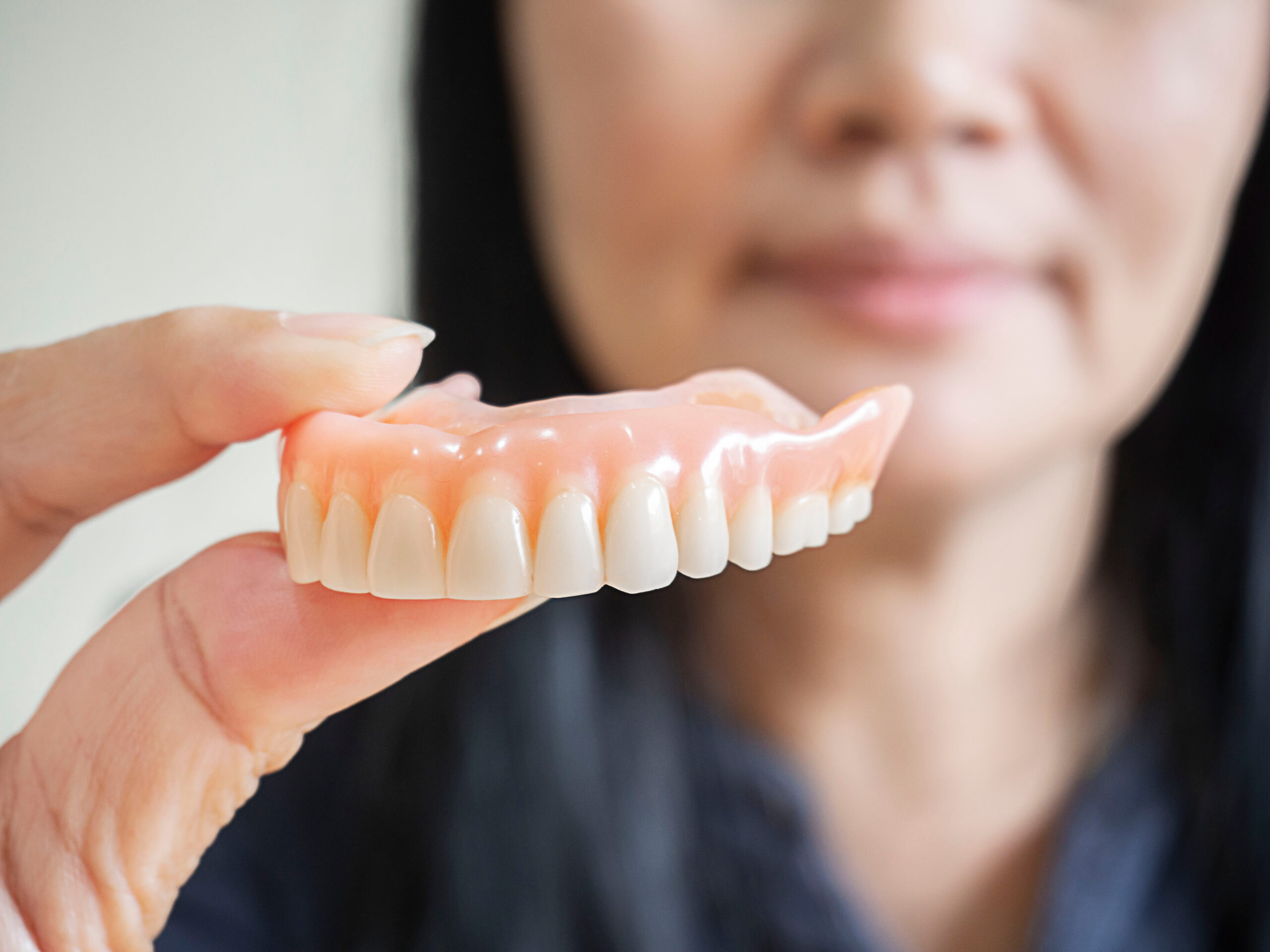 Happy asian woman be smile and holding dentures in hand. Dentures for prosthetic devices constructed to replace missing teeth and helping to chew food.