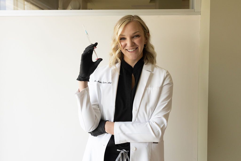 Female dentist in white coat and black shirt holding dental syringe, smiling
