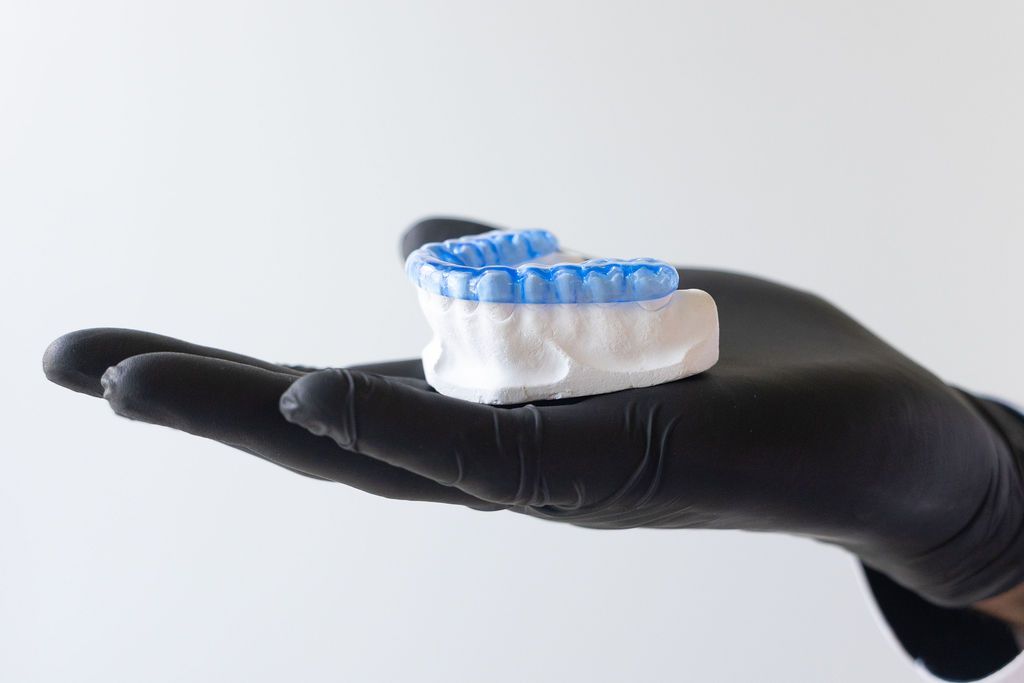 Dentist displaying clear aligner orthodontic device in black gloved hand