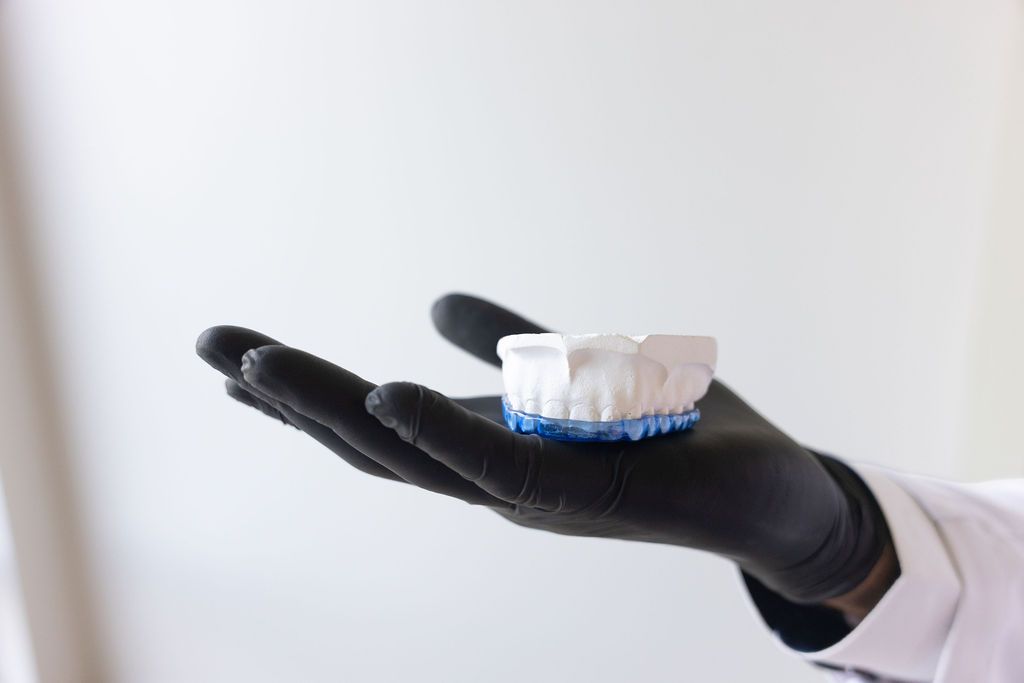 Dental professional holding clear aligner with blue base in gloved hand