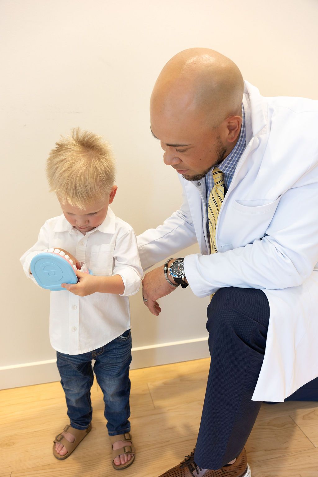 Pediatric dentist teaching child oral hygiene with blue toothbrush model
