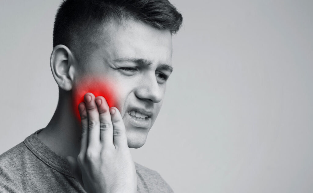 Teeth problem. Man suffering from strong tooth pain, monochrome photo with red inflamed zone, free space